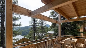 A wooden deck with tables and chairs, overlooking a forested valley.