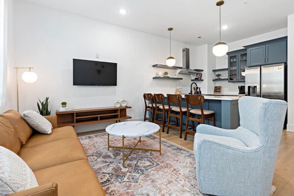 Ein modernes Wohnzimmer mit einer Couch, einem Couchtisch und einem Essbereich mit Stühlen, im Hintergrund befindet sich eine Küche.