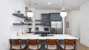 A modern kitchen with a central island, wooden chairs, and built-in cabinets. - Chic East Nashville Condo -Free Parking 3 miles to Broadway (Nashville)