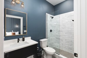 Ein Badezimmer mit weißem Waschbecken, dunklem Waschtisch, einer weißen Toilette und einer Duschkabine aus Glas.