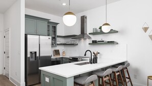 Une cuisine moderne dotée d’un îlot central, d’appareils électroménagers en acier inoxydable et de tabourets de bar.