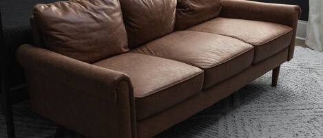 A brown leather sofa with wooden legs in a room with a dark wall and a white rug.