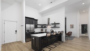 A modern kitchen with a central island, black bar stools, and a stainless steel refrigerator. - Luxury 6 Bed 3 Bedroom Walk to Restaurants +Coffee (Nashville)