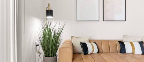 Una sala de estar moderna con un sofá de cuero, una planta en maceta y dos obras de arte abstractas enmarcadas en la pared.