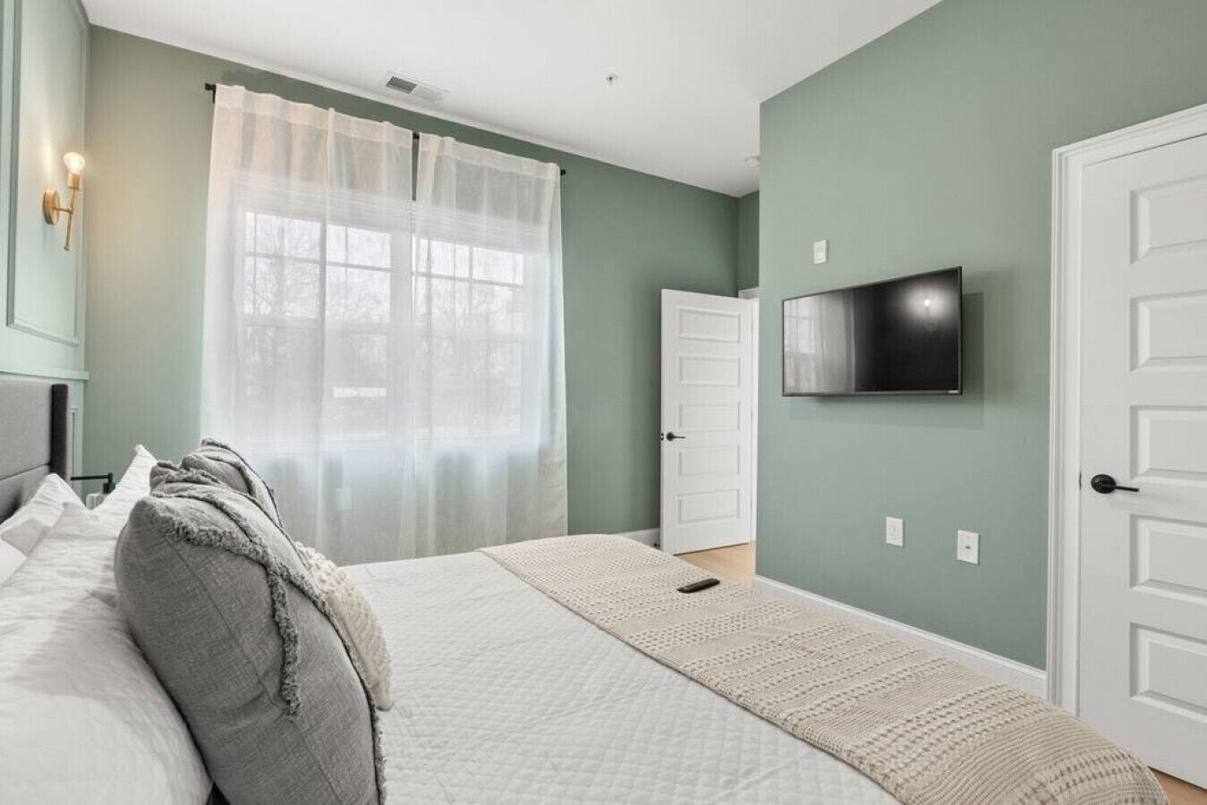 A bedroom with a bed, a TV mounted on the wall, and a door.