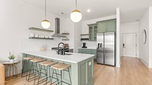 Una cocina moderna con una isla central, taburetes de bar, electrodomésticos de acero inoxidable e iluminación colgante.