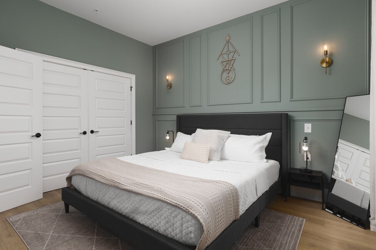 A bedroom with a bed, two bedside tables, a wardrobe, and a wall-mounted light fixture.