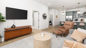 A modern living room with a flat-screen TV, a wooden console, a round woven ottoman, and a leather armchair. - Condo with Free Parking, 3 miles Downtown, near Restaurants (Nashville)