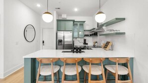 A modern kitchen with a central island, bar stools, and a refrigerator. - Chic and Cozy Designer Condo 3 Miles to Downtown (Nashville)