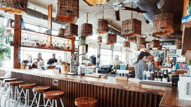 A bar with wooden stools, hanging wicker baskets, and a counter with various bottles and a cash register. - Chic and Cozy Designer Condo 3 Miles to Downtown (Nashville)