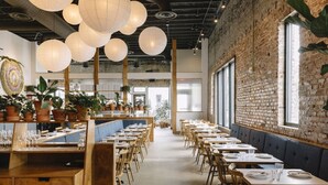 A restaurant with a long counter, wooden chairs, and tables set for dining. - Chic and Cozy Designer Condo 3 Miles to Downtown (Nashville)