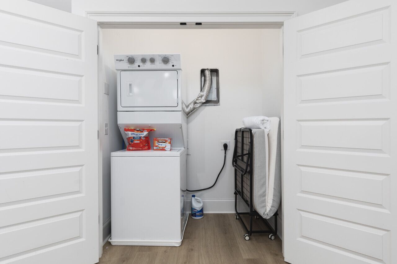 A laundry area with a stacked washer and dryer, a drying rack, and a water dispenser.