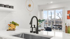 Een moderne keuken met een zwarte kraan, witte aanrechtbladen en uitzicht op het landschap door grote ramen.