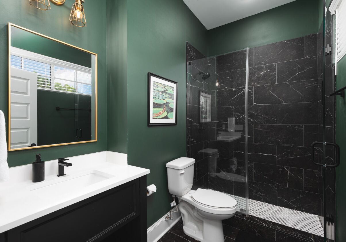 Un baño con lavamanos blanco, grifo negro y un inodoro blanco. Hay un cuadro en la pared y una ducha con azulejos negros.