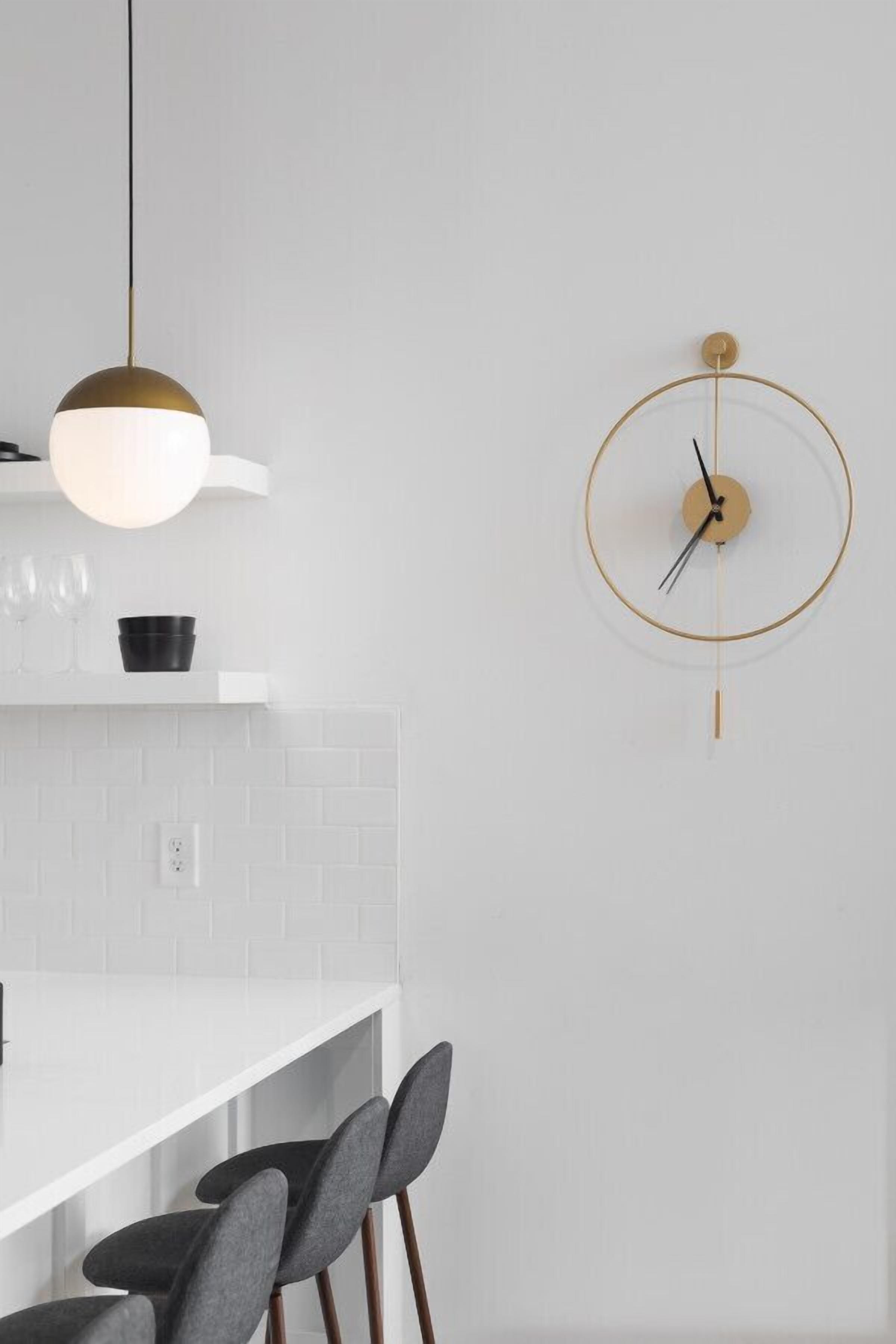 Eine moderne Küche mit weißer Arbeitsplatte, einer hängenden Pendelleuchte und einer an der Wand befestigten Uhr.
