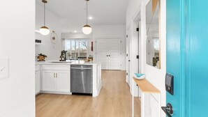 Een moderne keuken met witte kasten, een roestvrijstalen vaatwasser, hanglampen en uitzicht op het buiten.