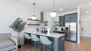 A modern kitchen with a central island, bar stools, a built-in oven, and a stainless steel refrigerator.