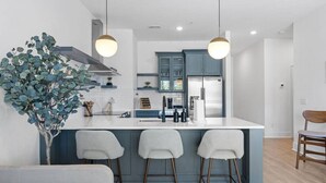 A modern kitchen with a central island, bar stools, and a dining area with a sofa.