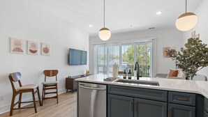 A modern kitchen with a central island, dark cabinetry, and a large window providing natural light.