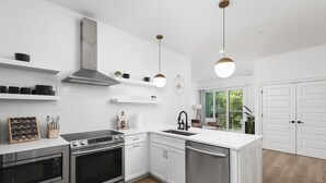 Uma cozinha moderna com armários brancos, eletrodomésticos de aço inoxidável e iluminação pendente.