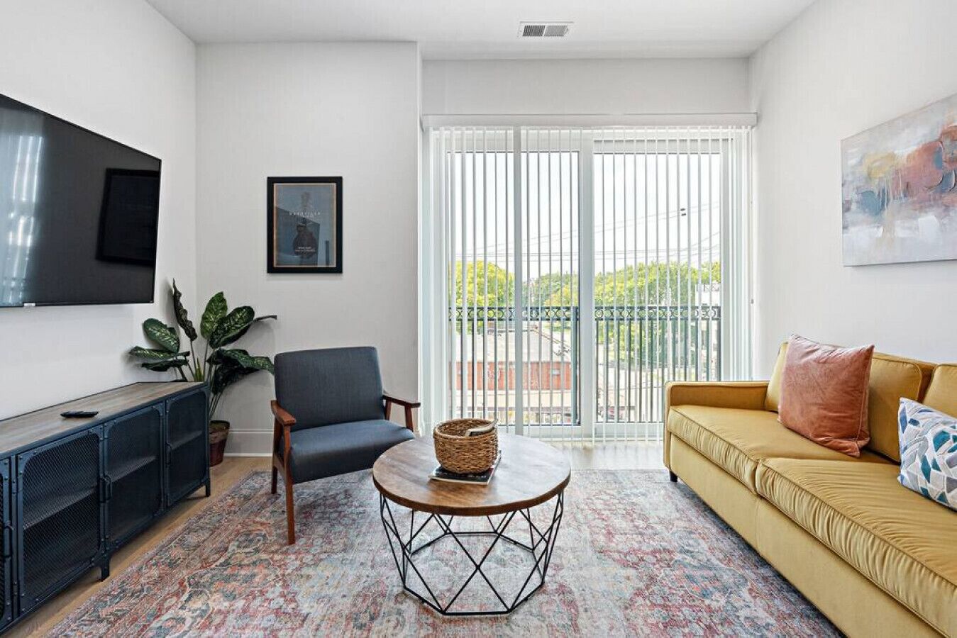 Un salón con sofá, sillón, mesa de centro, televisor y un ventanal con persianas.
