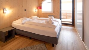 Un dormitorio moderno con techo de madera, una cama grande, una mesita de noche, una lámpara y un ventanal corredero que da a un espacio exterior.
