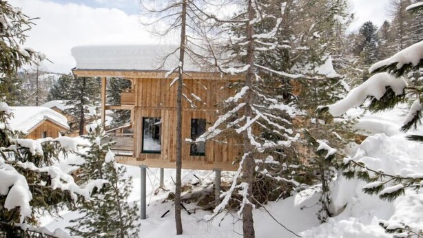 Una cabaña de madera con estructura de dos pisos, rodeada de árboles cubiertos de nieve.