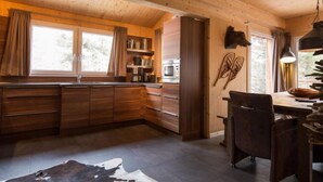A wooden interior with a kitchen area, a dining table, and a chair.