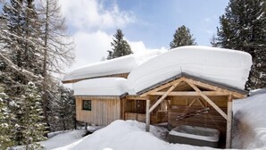 A snow-covered wooden cabin with a sloped roof and a wooden porch.