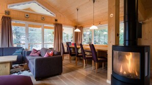 A cozy cabin interior with a sofa, dining table, chairs, and a wood-burning stove. - #23 mir IR-Sauna und Sprudelbad Innen by Interhome (Turracher Höhe)