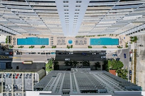 A high-rise building with two swimming pools, a parking area, and a view of the street below. - The Club- RE Rentals (Miami)