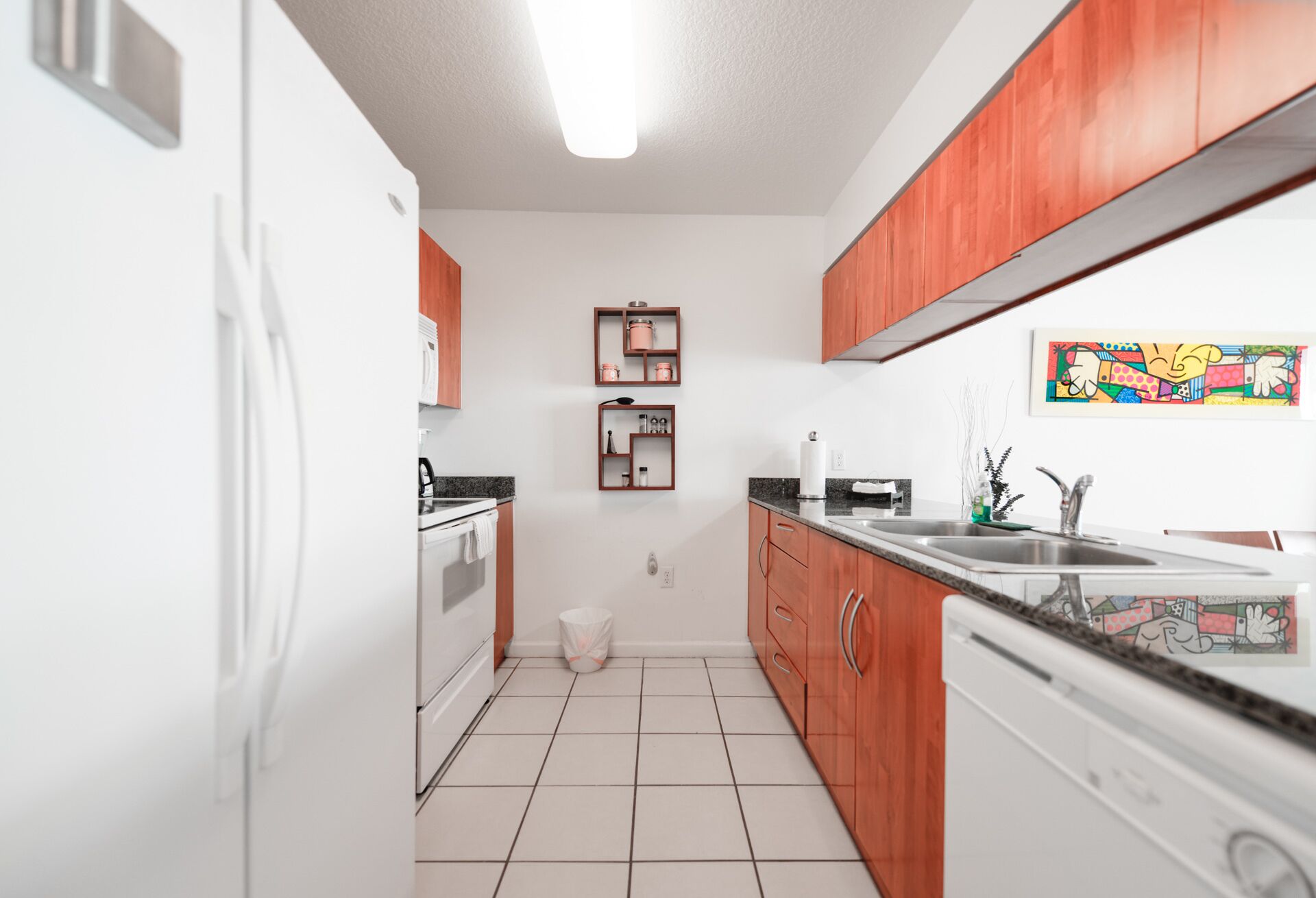 A compact kitchen with white cabinets, a stainless steel sink, and a colorful abstract painting on the wall.