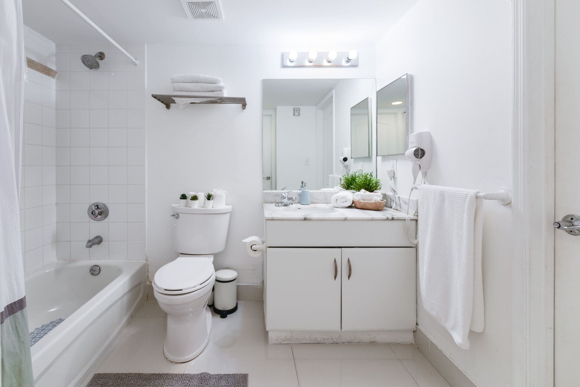 Une salle de bain moderne équipée d’une baignoire, de toilettes, d’un meuble-lavabo avec un miroir et d’un sèche-cheveux.