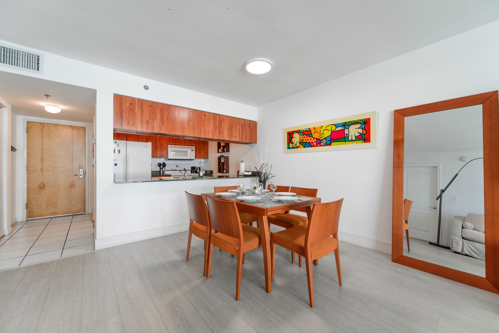 Une cuisine moderne avec des meubles en bois, une table à manger avec des chaises et un tableau abstrait aux couleurs vives accroché au mur.