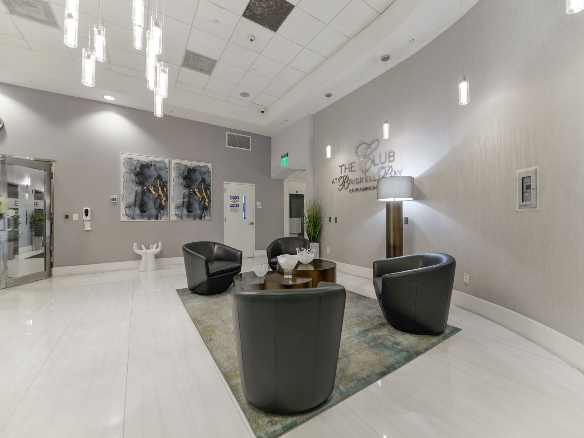 En modern entréhall med en receptionsdisk, två svarta läderfåtöljer, en vit skulptur och en väggmonterad skylt med texten "The Club at Brickell Bay".