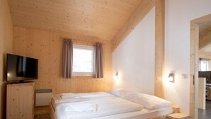 Ein Schlafzimmer aus Holz mit einem Bett, einem Fernseher und einem Fenster mit Vorhängen.