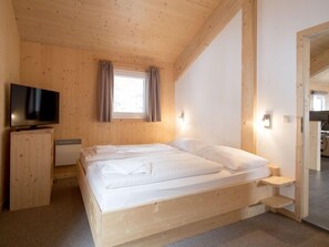 Un dormitorio de madera con una cama, un televisor y un ventanal con cortinas.