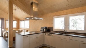 Eine moderne Küche mit Holzwänden, einer zentralen Kochinsel und großen Fenstern.