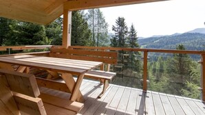 Eine Holzterrasse mit Picknicktischen und Bänken mit Blick auf eine bewaldete Berglandschaft.