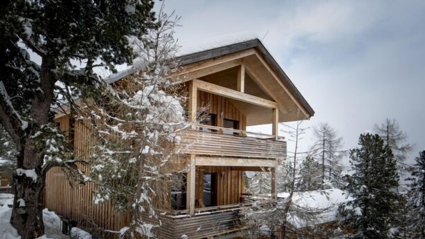 Eine Holzhütte mit einem Balkon, umgeben von schneebedeckten Bäumen.