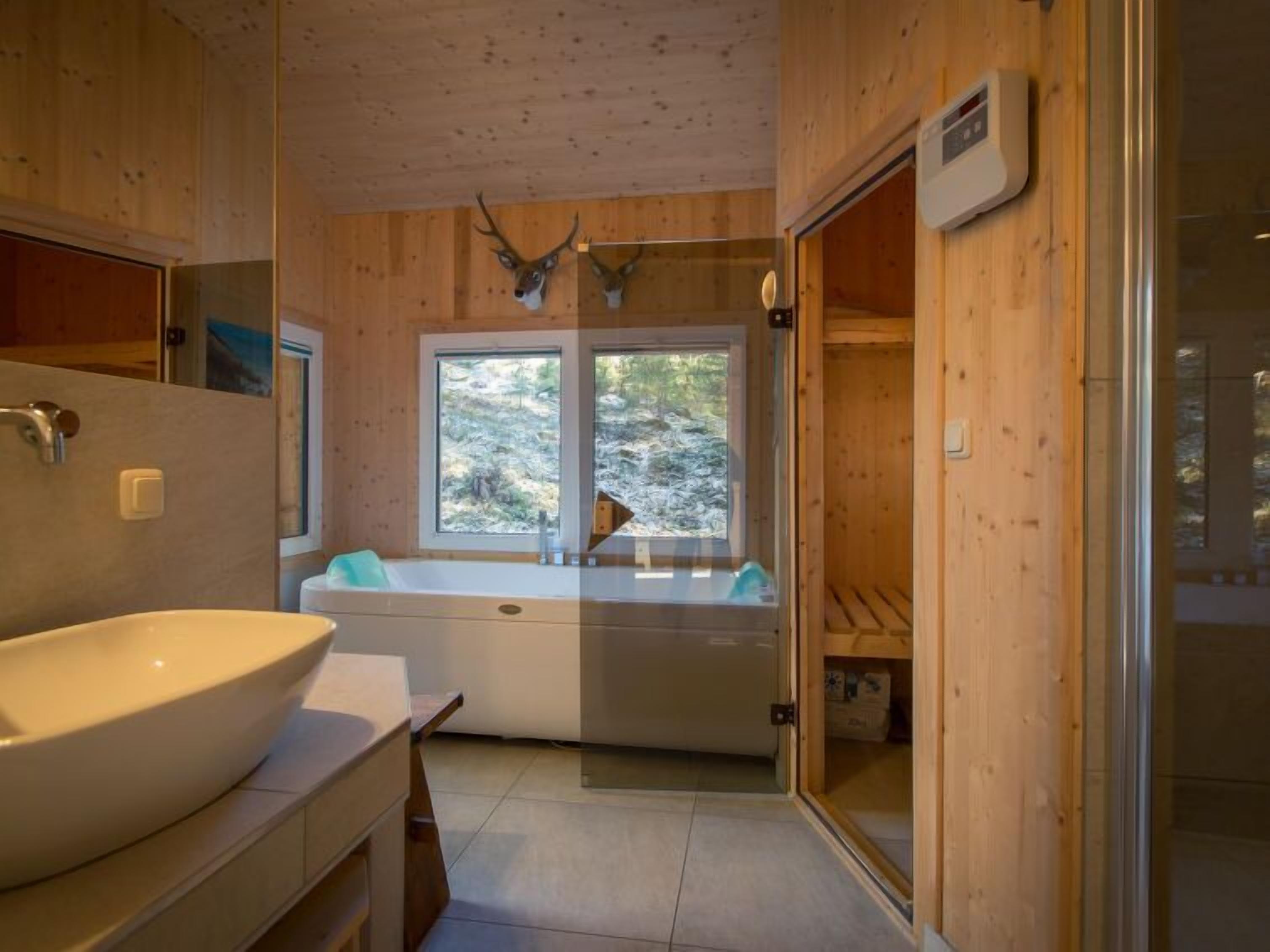 Ein Badezimmer mit einem großen Waschbecken, einer Badewanne und einem Fenster mit Blick auf Bäume.