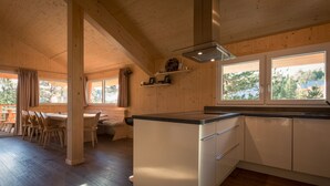 Cozinha moderna com paredes de madeira, área de refeições com cadeiras e grandes janelas.