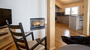 Un salon moderne doté d’une cheminée, d’un téléviseur et d’un coin repas, avec un plancher en bois et une cuisine en arrière-plan.