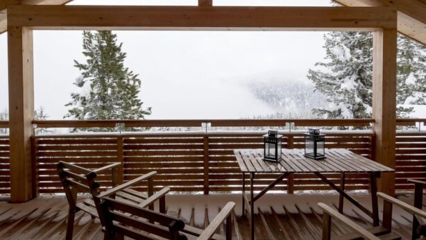 Une terrasse en bois, agrémentée de bancs et de tables, qui offre une vue sur un paysage enneigé et boisé.