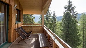 A wooden cabin with a balcony, a bench, and a chair.