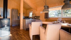 A cozy cabin interior with a wooden interior, a dining area with chairs, a kitchen with a stove, and a large window providing natural light.