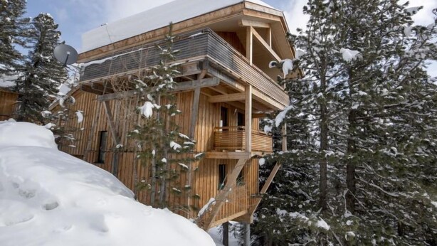 A wooden chalet with a balcony, surrounded by snow-covered trees.