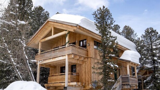A wooden chalet with a balcony, surrounded by snow-covered trees.