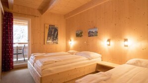 A wooden room with two beds, a window with curtains, and wall-mounted lights.