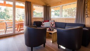 A cozy cabin interior with a sofa, two armchairs, a small table, and a window overlooking a wooden deck.